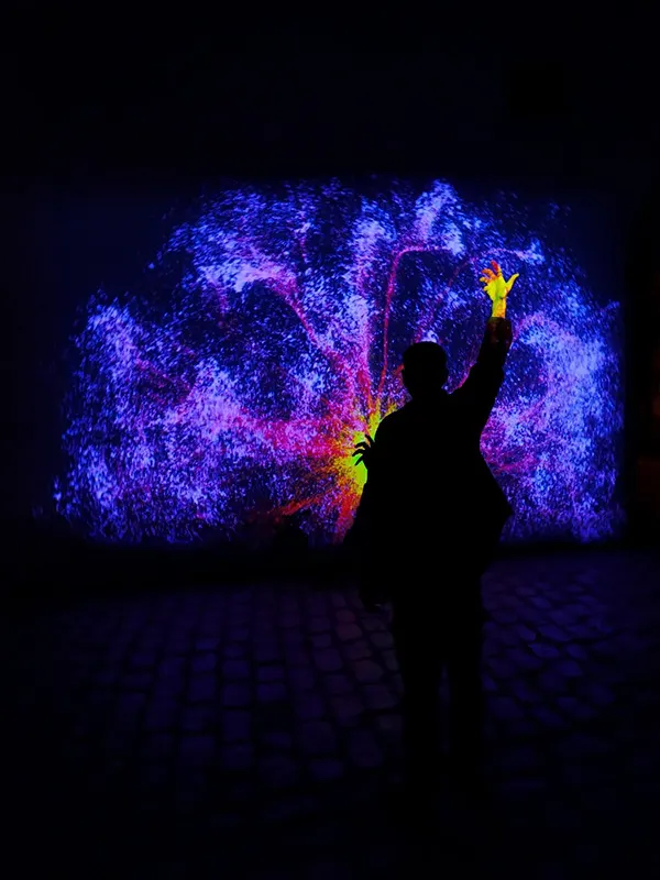 Visitor raising an arm in front of a wall of blue and violet particles that flare around the hand