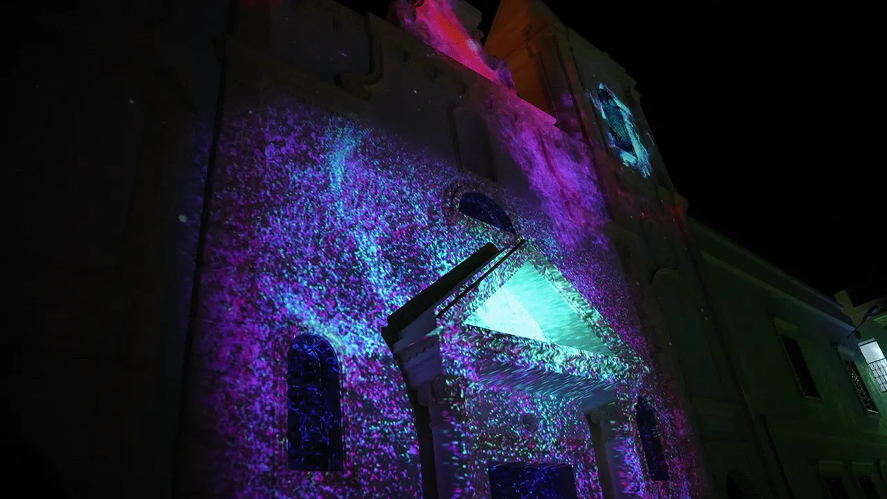 Violet particles spreading across the facade with a teal glow at the door