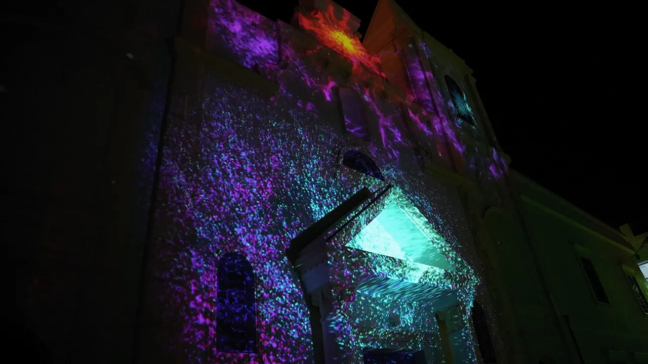 Projection of violet and teal particles with a red spiral near the top of the facade